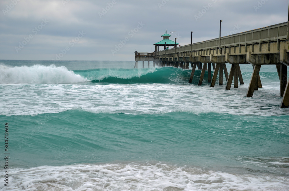 Wooden fishing pier with beach and waves in Atlantic Ocean in Florida