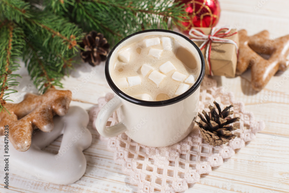 Hot Christmas drink with marshmallows in an iron mug and gingerbread cookies, on a white table. New Year, holiday background, copy space. Hot Christmas drink with marshmallows in an iron mug and gingerbread cookies, on a white table. New Year, holiday background, copy space.