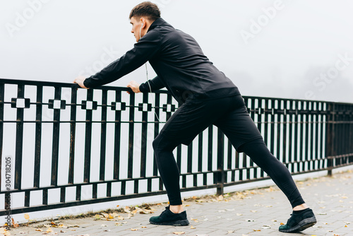 Rear view of an athletic muscular man stretching outdoor in the morning on the fog nature background. Fitness male exercising in the park. People and sport concept