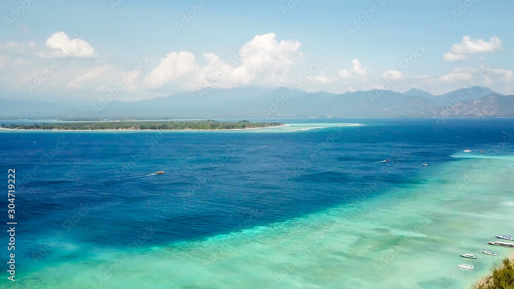 A drone shot of white sand beach on Gili Air, Lombok, Indonesia. Beautiful and clear sea water. There is a boat anchored to the beach. In the back visible Mount Rinjani. Holidays paradise.