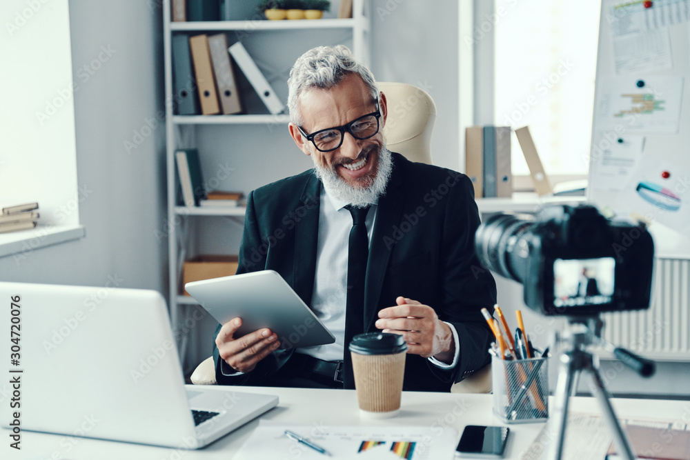 Confident mature man in elegant suit telling something and smiling while making social media video Confident mature man in elegant suit telling something and smiling while making social media video