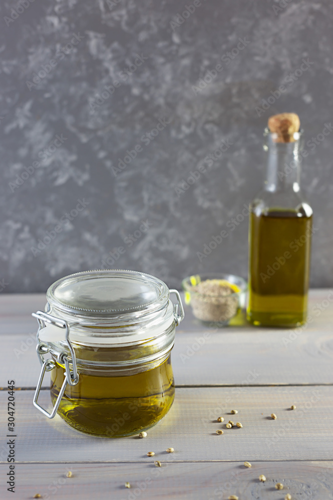 Hemp oil in a glass bottle, seeds and flour on a gray wooden background. Vertical photo.