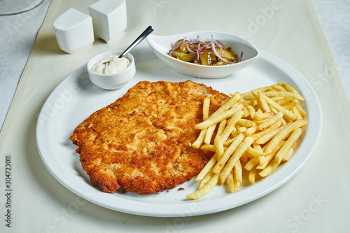 Fried schnitzel with french fries, sauces and salad on a white plate. Restaurant serving food. Flat lay
