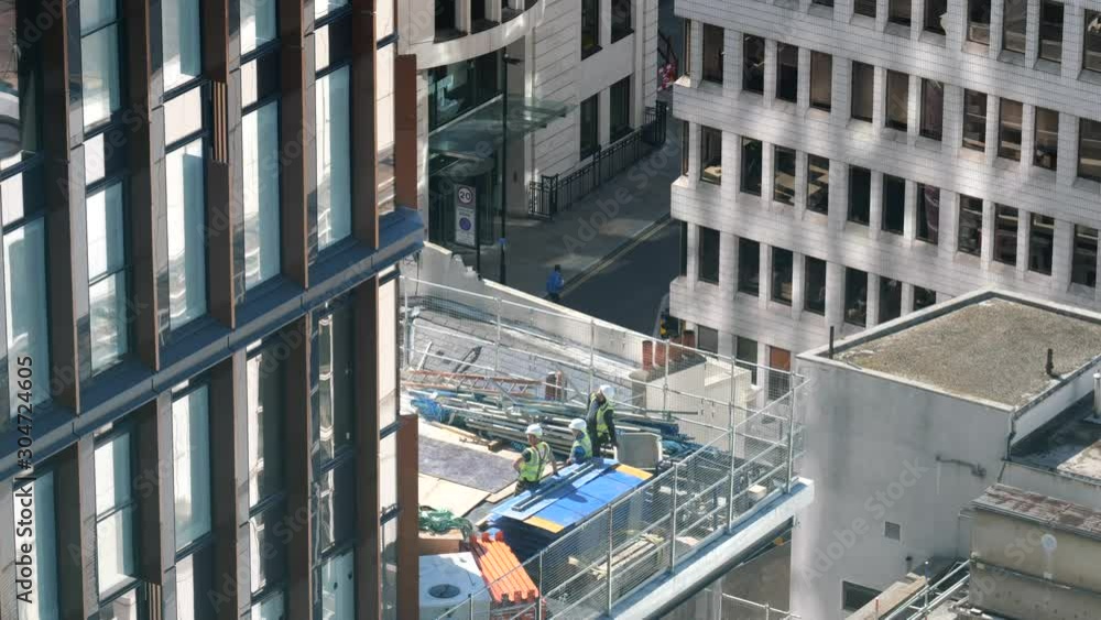 Three construction workers on a roof inside a site on a building in London with sun, high angle Three construction workers on a roof inside a site on a building in London with sun, high angle