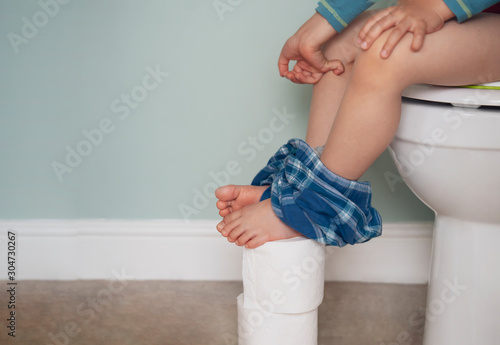 kid pinching fingers to help with stomach ache, Child boy having with bad tummy problem and diarrhea,Low view of  legs hanging with blue pajamas on white tissue, Training child or Health care concept