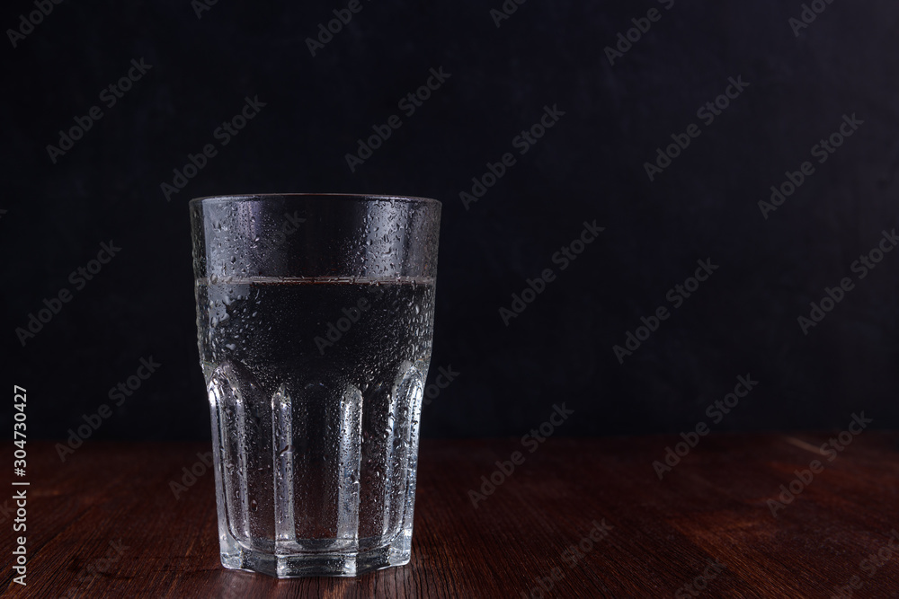 Glass of water with water drops on a wooden table with dark background. With copy space. - obrazy, fototapety, plakaty 