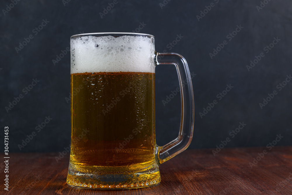 Mug of beer on wooden table on dark background