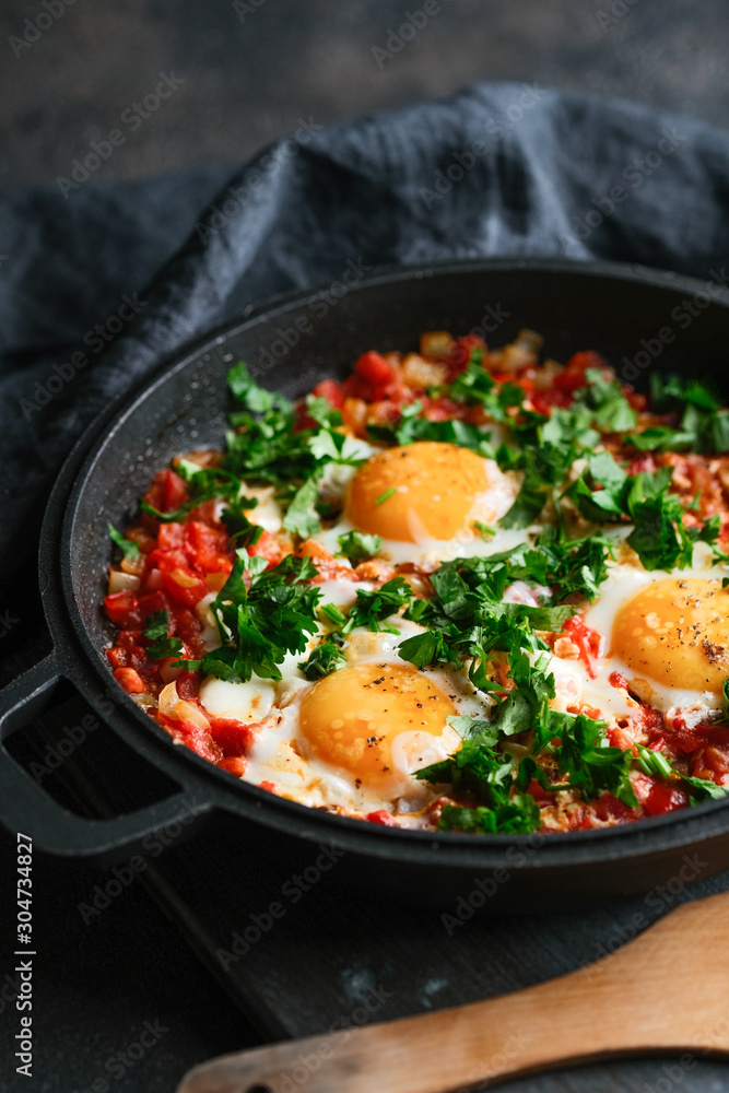 Traditional shakshuka with eggs, tomato, and parsley in a iron pan on a dark background Traditional shakshuka with eggs, tomato, and parsley in a iron pan on a dark background