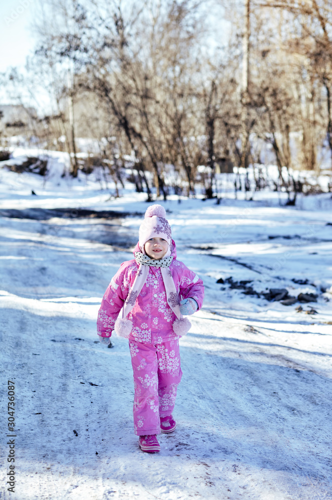 Little kid girl in colorful clothes playing outdoors. Active leisure with child in winter on cold days. Happy child having fun with snow