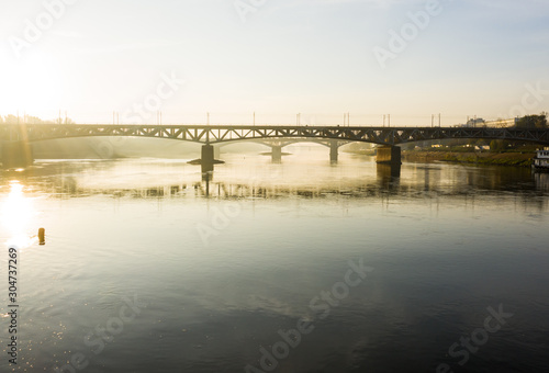 Drone flies to a railway bridge passing over the Vistula River in Warsaw. Poland. 04. October. 2019.  Aerial view of a bridge in the fog in the early morning at sunrise. © Oleksandr