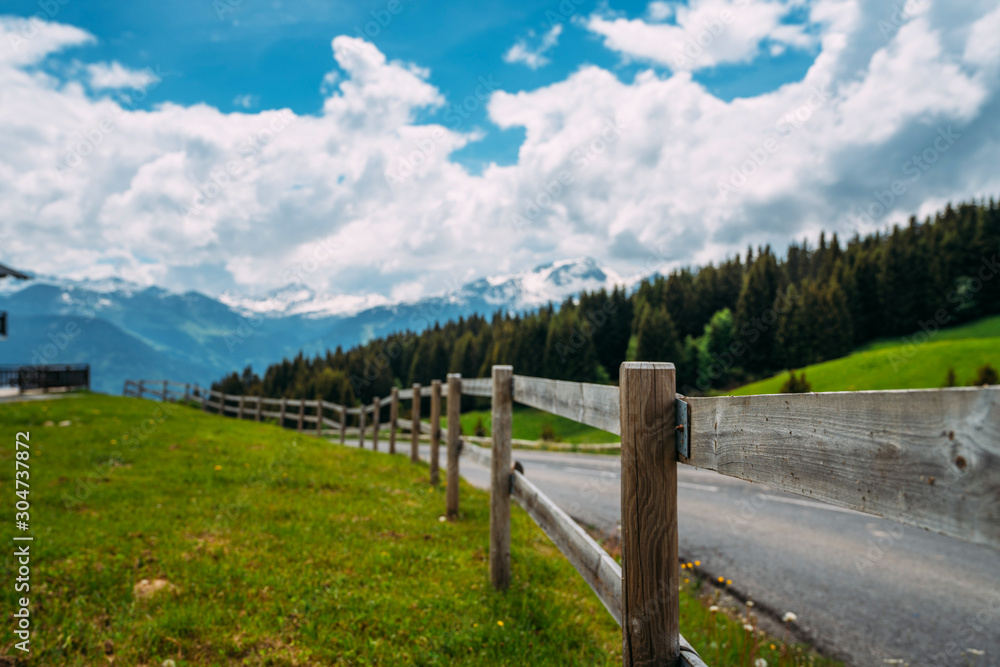 Vintage fence and countryside road in Swiss Alps. Summer green rural farm landscape.