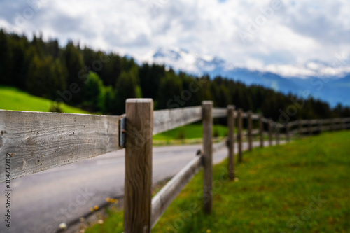 Vintage fence and countryside road in Swiss Alps. Summer green rural farm landscape.