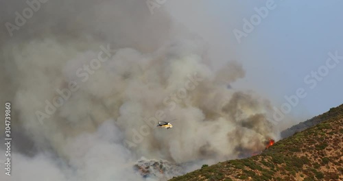 The dramatic view of destroying wildfire on Hollywood hills, near the Warner Bros studio. The hillside forest is in fire. Firefighting helicopter is involved in extinguishing a fire. photo