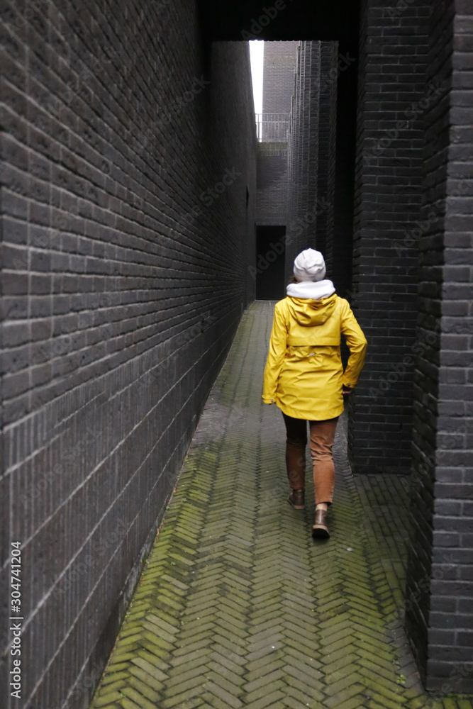 a girl in a yellow jacket walks down a dark black brick hallway a girl in a yellow jacket walks down a dark black brick hallway
