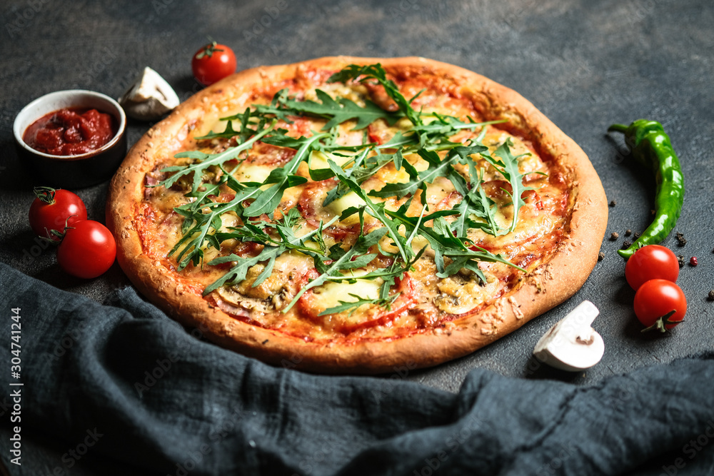 Traditional Italian pizza with ham, arugula, mozzarella, basil and tomatoes on a dark background copy space.