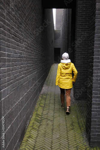 a girl in a yellow jacket walks down a dark black brick hallway
