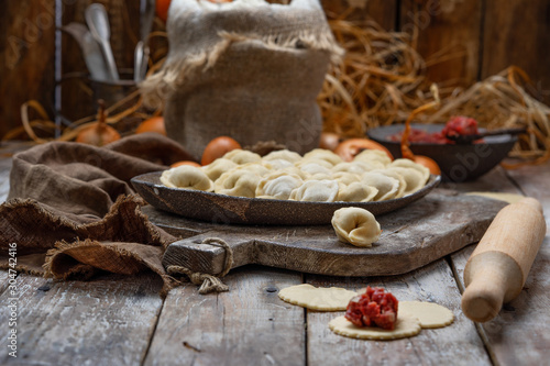 uncooked meat dumplings - russian pelmeni on cutting board and ingredients for homemade pelmeni on wooden table. Process of making pelmeni, ravioli or dumplings with meat
