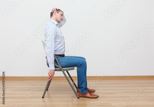 Caucasian man, sitting on chair, stretching neck - profile