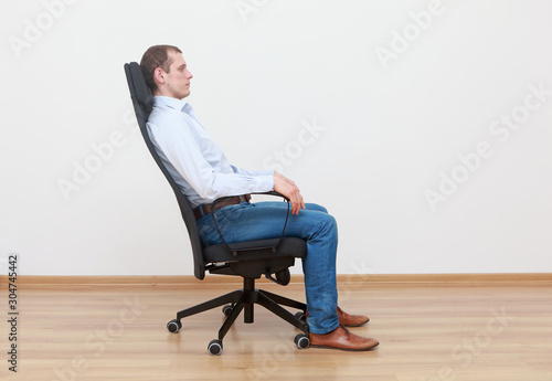 caucasian man sitting on the edge of office chair in relaxed position