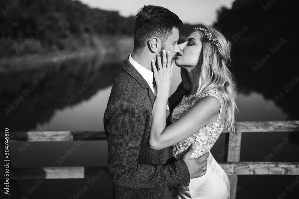 Black and white foto stylish couple of newlyweds posing on a bridge on wedding day. Handsome bearded groom admires and kisses pretty bride. Together. The concept of youth, love, fashion and lifestyle. Black and white foto stylish couple of newlyweds posing on a bridge on wedding day. Handsome bearded groom admires and kisses pretty bride. Together. The concept of youth, love, fashion and lifestyle.