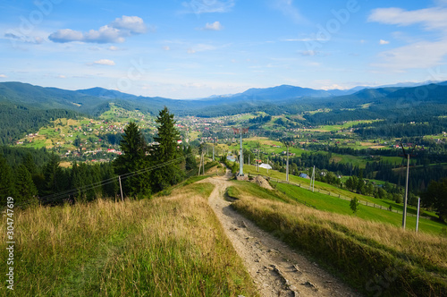 Dirt road in a village leads to the town in mountains. Countryside road and wide view of small town in a valley and mountains around. Vorokhta  Carpathian mountains  Ukraine.