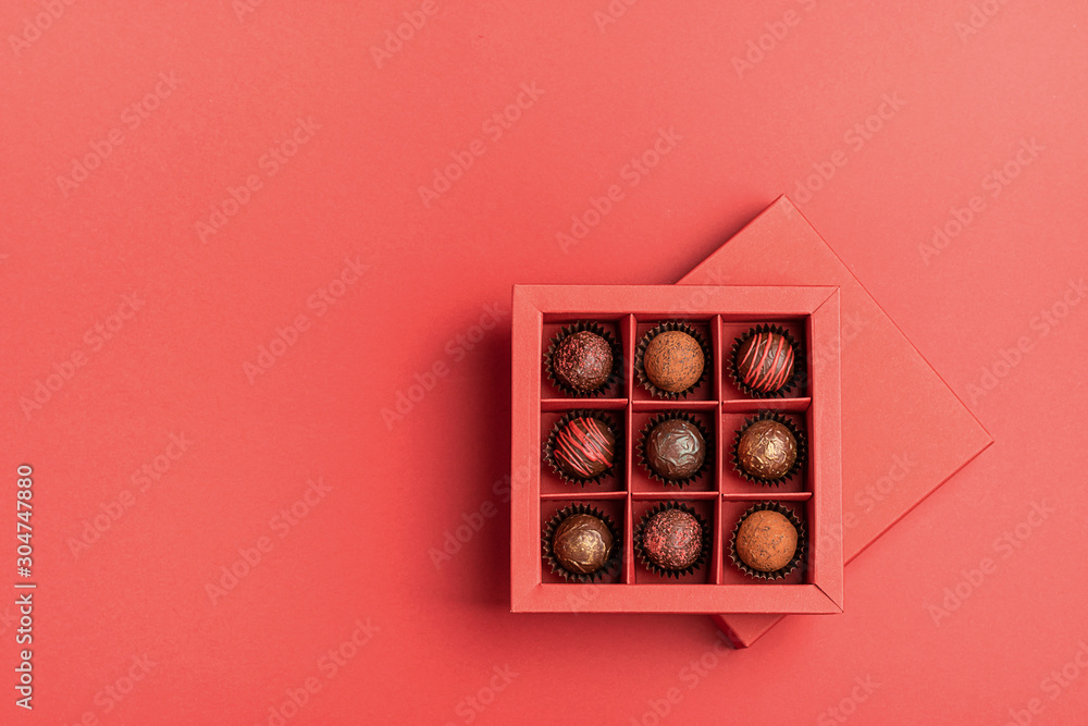 Chocolate candies in a red craft box on a bright coral background. Flat layout . Holiday Concept Chocolate candies in a red craft box on a bright coral background. Flat layout . Holiday Concept