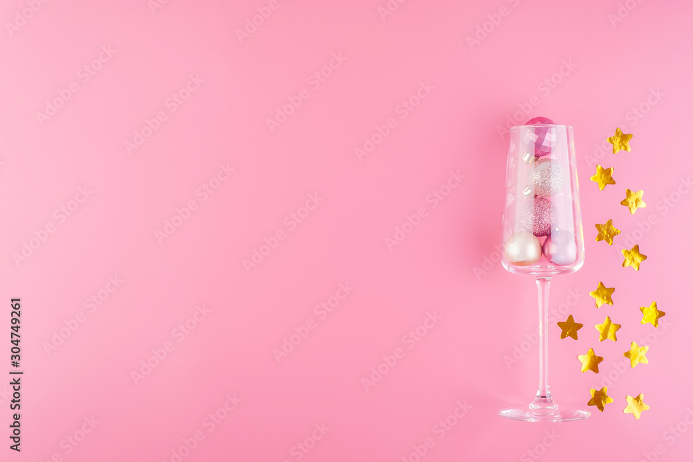A glass of champagne is filled with pink and gold shiny decorations in the form of balls on a pink pastel background A glass of champagne is filled with pink and gold shiny decorations in the form of balls on a pink pastel background