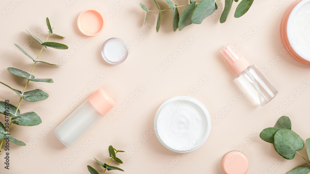 Organic cosmetic products on beige background. Flat lay composition with hand cream in jar, essential oil, skin lotion and eucalyptus leaves. Natural organic beauty product concept