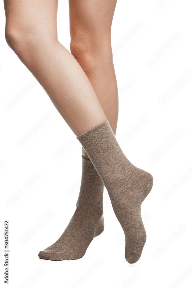 Cropped shot of a girl's cross legs, staying on a white background. It is dark beige socks on her foots. Cropped shot of a girl's cross legs, staying on a white background. It is dark beige socks on her foots.