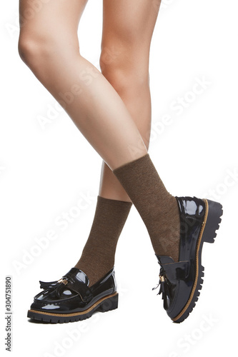 Cropped shot of a girl's cross-legs in black shoes, staying on a white background. It is brown-and-grey socks on her foots. 