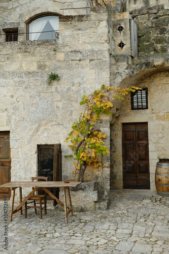 Vine plant grown in a stone planter in the Sassi of Matera. Courtyard of a house with a wooden table and a wine barrel.
