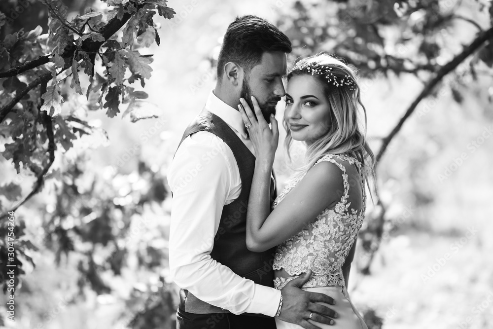 Sensual Black and white foto of bride and groom. Stylish couple of happy newlyweds posing and kisses in the park on their wedding day. Together. The concept of youth, love, fashion and lifestyle. 
