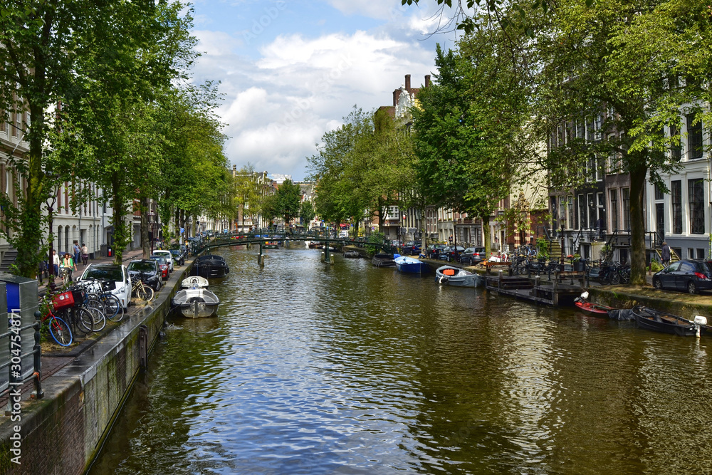 Amsterdam, Holland. August 2019. Classic view of a canal in the city: moored boats, the tree-lined avenue with bikes, the bridges that cross the canal.