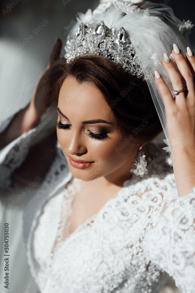 Beautiful bride portrait wedding makeup and hairstyle, girl in diamonds tiara and marriage robe, fashion bride gorgeous beauty, smiling happy bride portrait. The bride touches the crown Beautiful bride portrait wedding makeup and hairstyle, girl in diamonds tiara and marriage robe, fashion bride gorgeous beauty, smiling happy bride portrait. The bride touches the crown