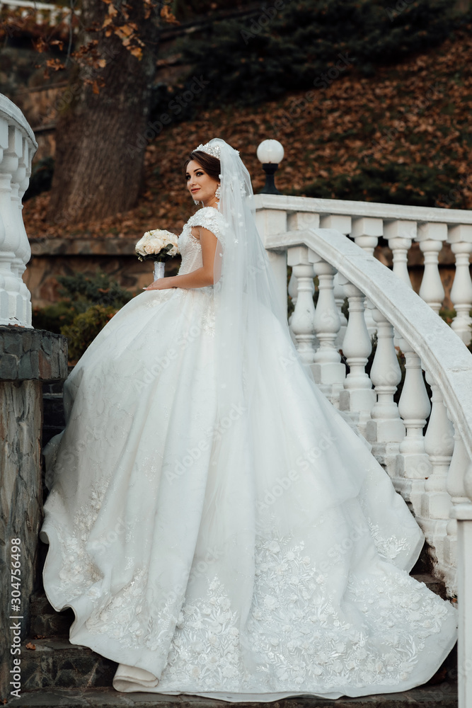Graceful bride climbs the stone stairs in a wedding dress with a train. Fashion photo of young bride. A bride go to the groom before the wedding ceremony. The first meeting of the newlyweds. 