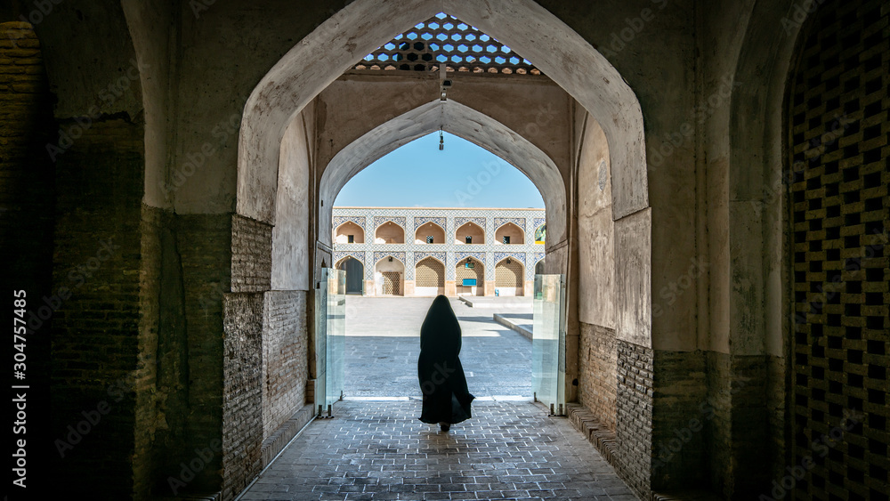 Unidentified woman in hijab walking towards the courtyard of the Great Mosque of Jameh Mosque of Isfahan, Iran