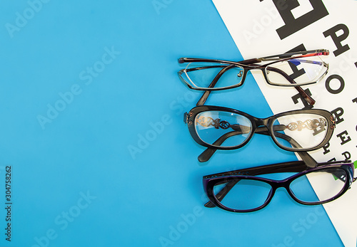 Eye glasses on eyesight test chart background close up. Blue backdrop. Flat lay.