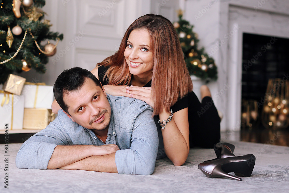 Beautiful young couple next to the Christmas tree. A young woman and a man are smiling and having fun together. Beautiful young couple next to the Christmas tree. A young woman and a man are smiling and having fun together.