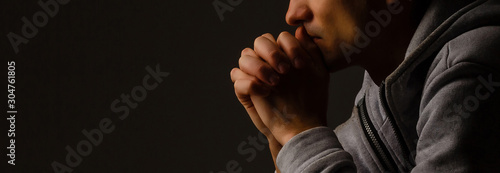 Obraz na plátně Religious young man praying to God on dark background, black and white effect