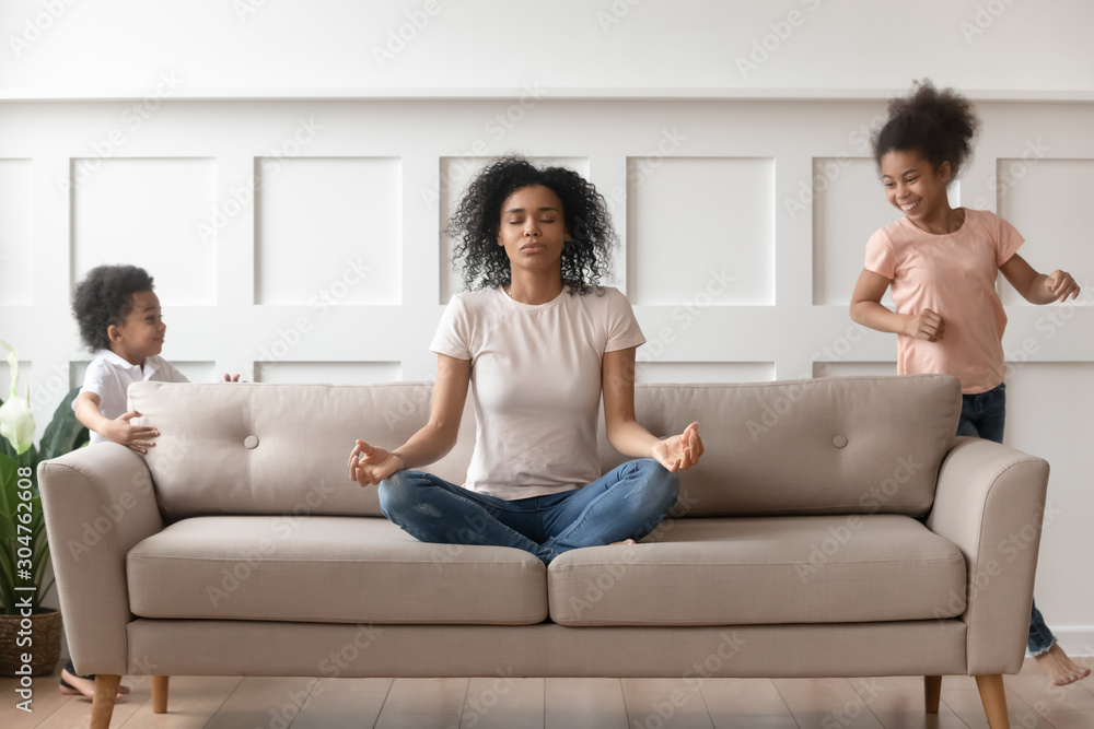 While noisy kids running young african mother meditates on couch While noisy kids running young african mother meditates on couch