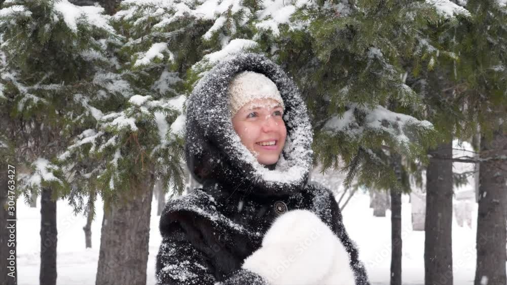 Happy Smiling Beautiful Woman Looking Up and Enjoying Snowfall Staying in Winter Frosty Park with Snow Trees in Fur Coat with White Gloves. Concept of Winter Christmas Holidays Happy Smiling Beautiful Woman Looking Up and Enjoying Snowfall Staying in Winter Frosty Park with Snow Trees in Fur Coat with White Gloves. Concept of Winter Christmas Holidays