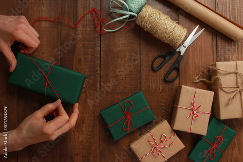 Hands of woman wrapping Christmas and New Year gifts. Present packing concept. Boxes, ribbons, strings, bows, scissors
