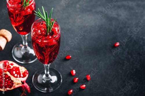Pomegranate Champagne Cocktail with rosemary on gray concrete stone background