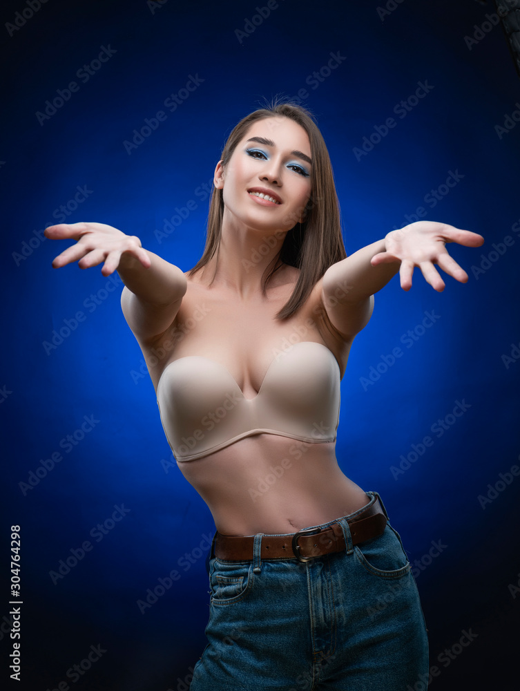 Beautiful mixed race Asian girl with big breasts, wearing a bra and jeans,  smiles and holds out her hands forward. Advertising, commercial design.  Stock Photo
