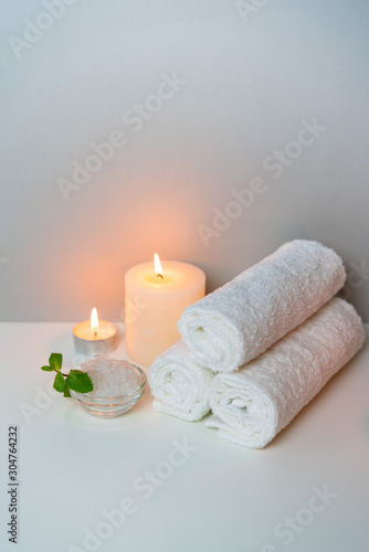 SPA procedure at salon vertical concept photo on grey background with stack of white towels, candles and cup of sea salt.