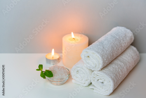 SPA procedure at salon concept photo on grey background with stack of white towels, candles and cup of sea salt.
