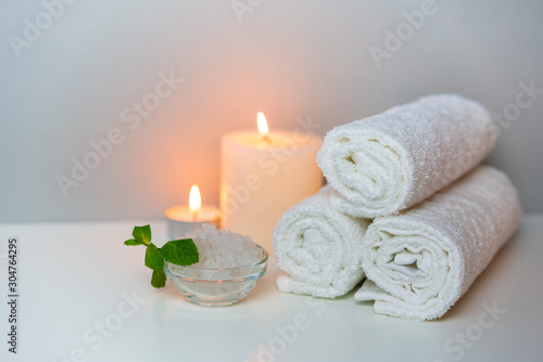 Natural health & SPA concept photo, horizontal orientation. Stack of white towels, candles light, sea salt prepared for salon procedure.