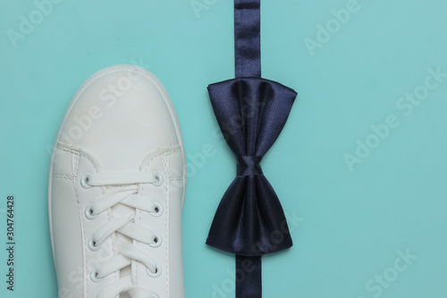 Minimalistic fashion still life, groom look. Stylish white sneakers and a bow tie on blue background. Top view