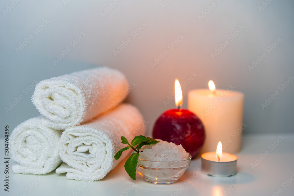 SPA day concept photo with candle lights, stack of towels and sea salt in a cup.