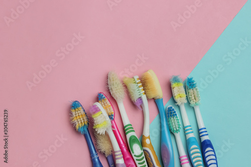 Lot of old used toothbrushes on a blue-pink pastel background  top view  minimalism